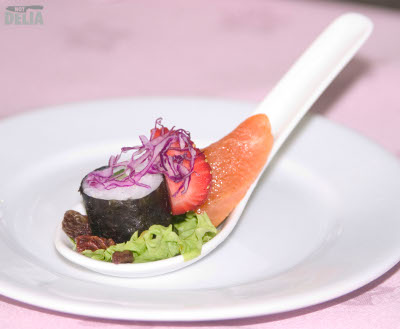A piece of smoked salmon with sashimi, salad, and a strawberry presented on a Chinese soup spoon