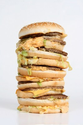 A burger tower with nine or ten burgers, processed cheese slices, soggy buns and sagging, tattered lettuce