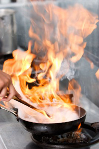 Fire blazes from a frying-pan as a chef flambés a dish