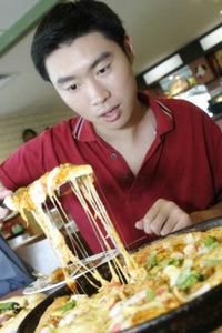A young Asiatic man lifts a slice of pizza from the pan