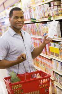 A man in a supermarket aisle, carrying a shopping basket and holding a list
