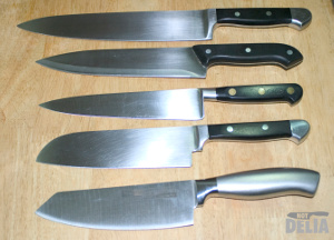 Five chef knives of various designs displayed on a wooden table