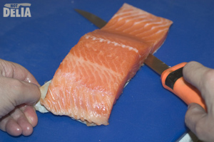 Filleting knife slicing between the skin and flesh of a fillet of salmon