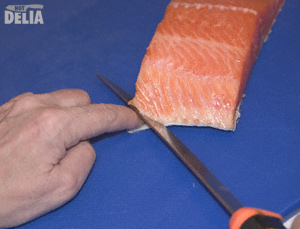 Filleting knife inserted between the skin and flesh of a fillet of salmon