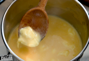 A "curd" of lightly scrambled egg on a wooden spoon above a saucepan