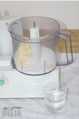Butter and flour in a food processor, with a glass of cold water to the side