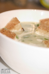 Close-up of a bowl of leek and potato soup with croutons and extra herbs