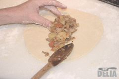 Pasty filling being spooned onto a circle of pastry and shaped