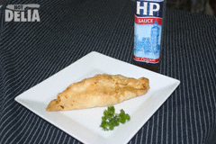 A meat pasty on a plate with a bottle of HP brown sauce to one side