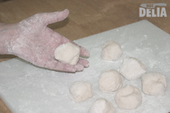 A hand holds a ball of dough, beside several more balls