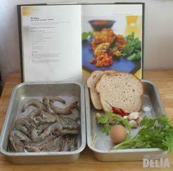 Prawns, bread, garlic, chillis, ginger, coriander and egg in two aluminium trays, with an open cookbook behind