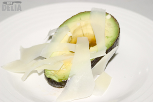 Half an avocado, drizzled with vinaigrette and topped with Parmesan cheese shavings