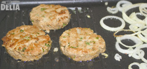 Not Delia's beef burgers sizzling on the griddle with some onions Beef burgers and onion rings frying on an electric griddle
