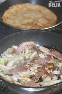 Bacon, mushrooms, leek and garlic all cooking together in one pan, with a buckwheat pancake frying in another