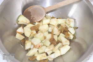 Apple pieces, ground cinnamon and sultanas in a steel mixing bowl with a wooden spoon