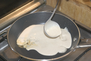 Batter being poured into a small frying-pan with a ladle