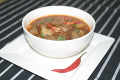 Goulash soup with a sprinkling of coriander and red chilli slices in a white bowl on a white plate
