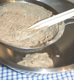 Pieces of pork liver being squeezed through a steel wire sieve into a steel bowl
