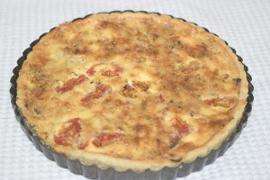 A quiche in its baking tin, just after emerging from the oven