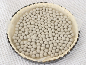 A layer of pastry fitted into a quiche tin, with ceramic baking beans across the surface
