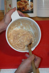 Chicken pieces in a bowl with marinade, being stirred with a wooden spoon