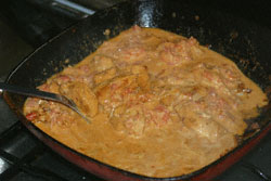 Fried marinated chicken pieces being further cooked in a tomato and butter mixture in a frying pan