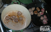 Beef cubes being browned in very hot oil in a cast iron casserole