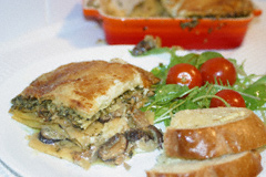Mushroom and pesto lasagne on a plate with rocket and tomato salad and some garlic bread