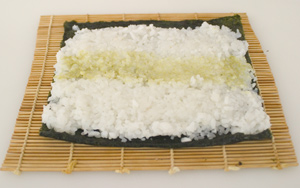 A sheet of nori on a makisu, spread with a layer of sushi rice and with a thin strip of wasabi