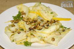 Thinly-sliced strips of yellow courgette or zucchini with toasted pinenuts, lime juice and coriander on a white plate