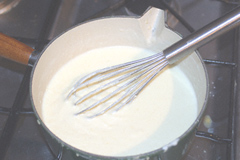 Béchamel sauce cooking in a cast-iron saucepan with a whisk