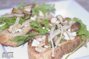 Two slices of bruschetta with feta cheese, mushrooms and herb leaves