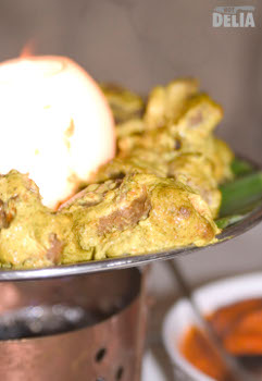Tandoori lamb tikka and an onion lamp on a steel platter above a small copper brazier