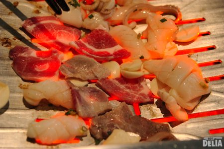 Pork neck and squid cooking in a tabletop barbecue