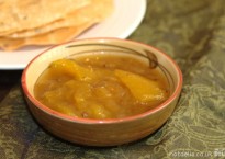 A dish of mango chutney with some poppadoms